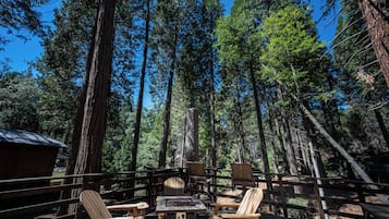 A wooden deck with outdoor seating and a fire feature, surrounded by tall trees.