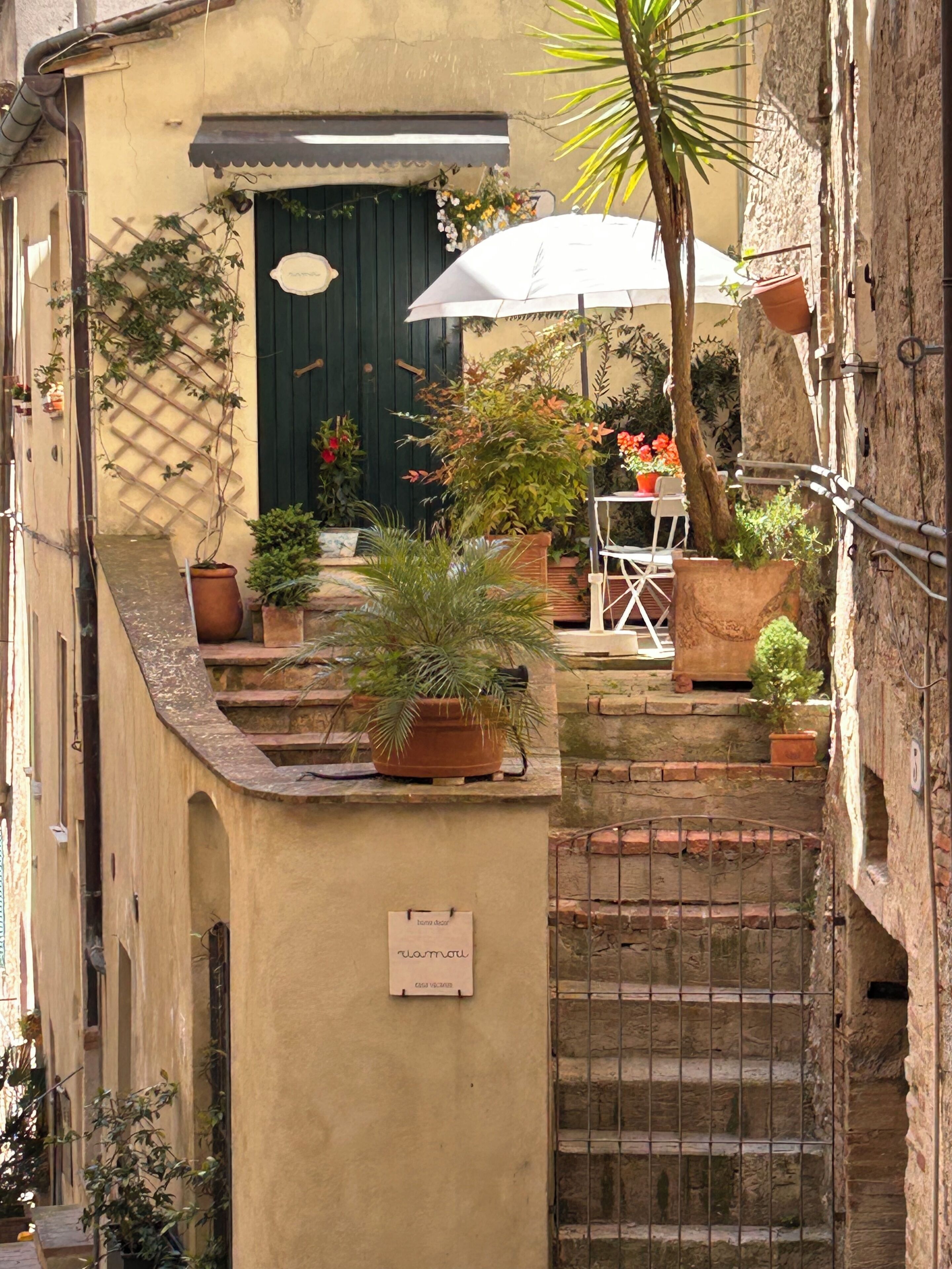 A narrow alley with a small outdoor seating area, a staircase, and potted plants.
