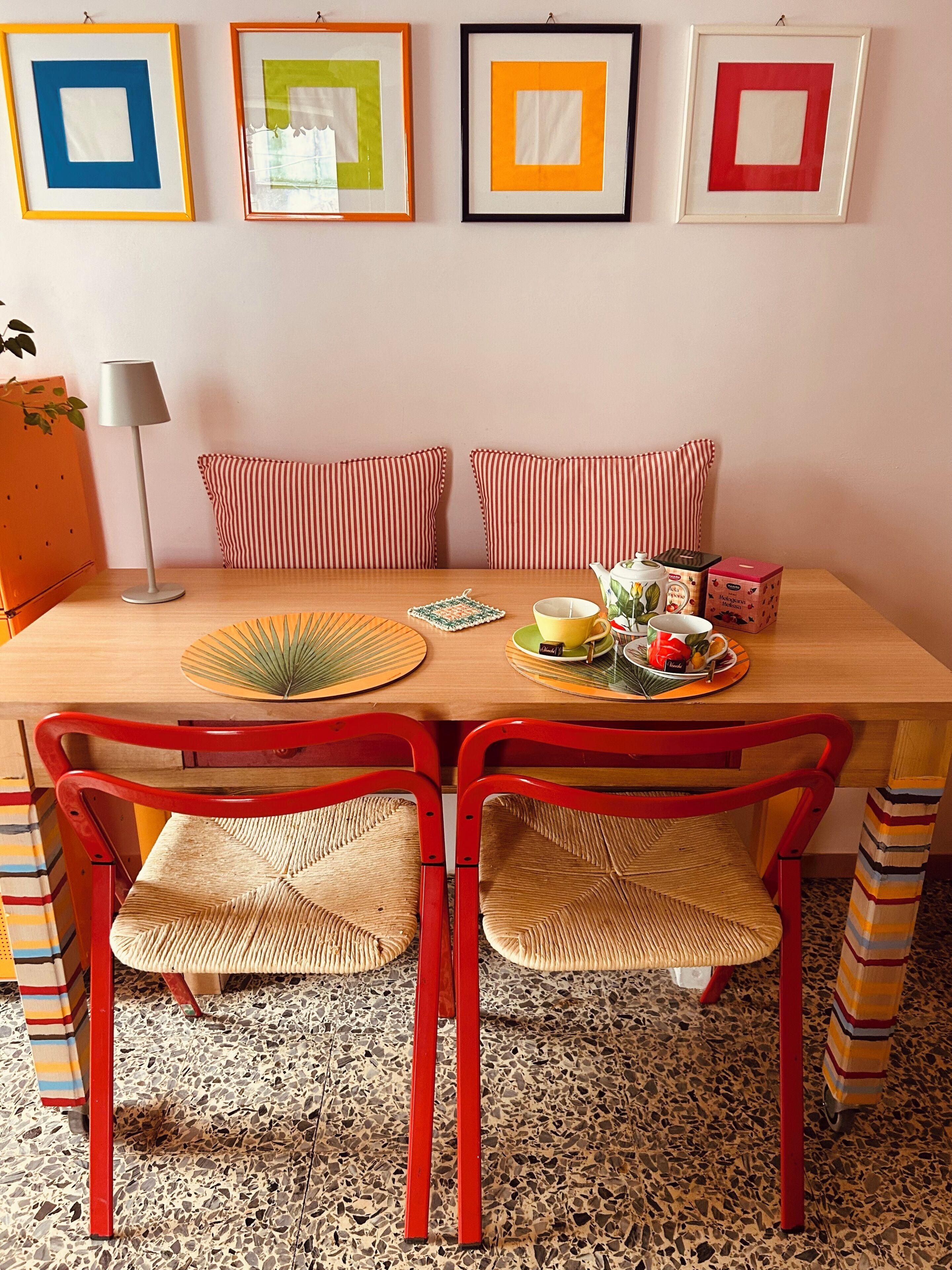 Ein Essbereich mit einem Holztisch, roten Stühlen und gerahmten Kunstwerken an der Wand.