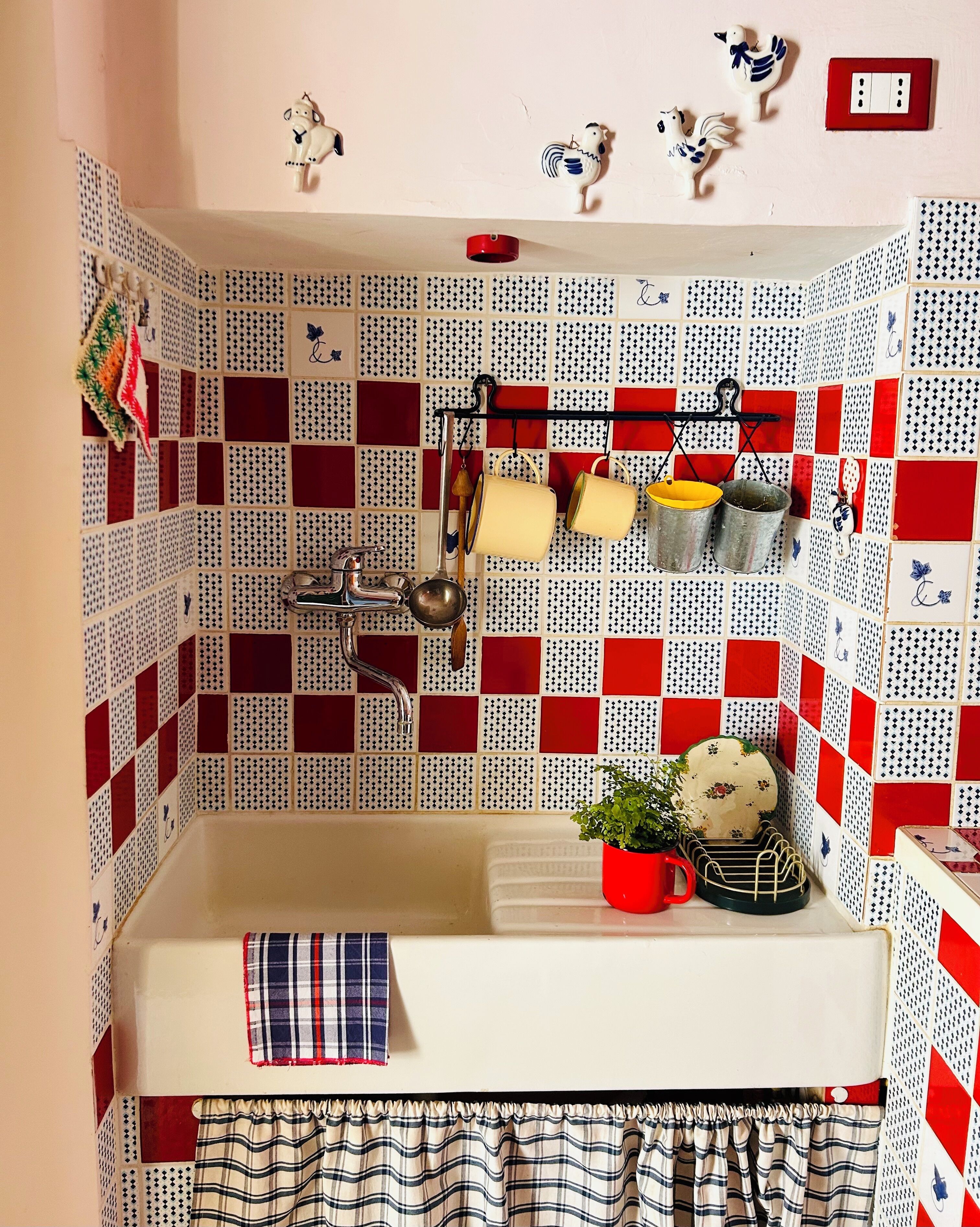 A kitchen with a checkered backsplash, a sink, and various kitchen utensils.