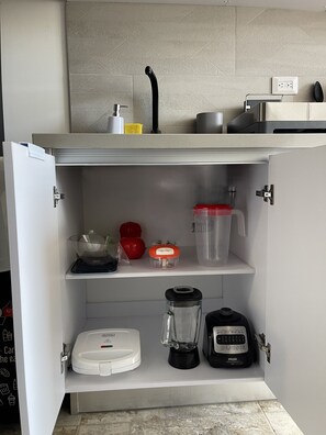Eine Küche mit einem weißen Kühlschrank, einer Kaffeemaschine, einem Mixer und einem Wasserkocher auf der Arbeitsfläche.