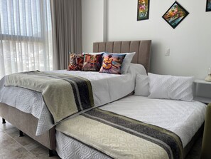 Ein Doppelbett mit Kopfteil, zwei Kissen mit tropischem Muster und ein Nachttisch mit Lampe.