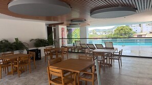 Ett rymligt utomhusområde med plats för måltider, med träbord och stolar, en pool i bakgrunden och utsikt över det omgivande landskapet.