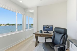 Ein Zimmer mit Schreibtisch, Stuhl und großem Fenster mit Blick auf ein Gewässer.