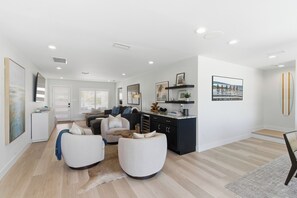 A spacious living area with a sofa set, a dining table, and a kitchen area with a black countertop. - Coastal Reserve Executive Beach Home w/ golf cart (Indian Rocks Beach)