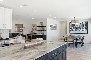 A modern kitchen with a marble countertop, a dining area with a wooden table and chairs, and a living area with a sofa and a coffee table. - Coastal Reserve Executive Beach Home w/ golf cart (Indian Rocks Beach)