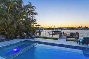 A swimming pool with lounge chairs and a view of boats and a marina at sunset. - Coastal Reserve Executive Beach Home w/ golf cart (Indian Rocks Beach)