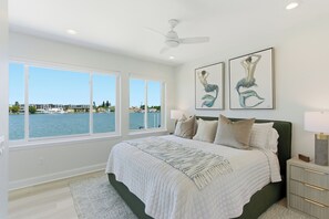 A bedroom with a large bed, two windows, a ceiling fan, and artwork. - Coastal Reserve Executive Beach Home w/ golf cart (Indian Rocks Beach)