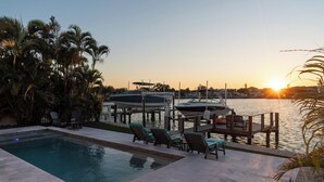Una piscina con lettini e vista su barche sull'acqua al tramonto.
