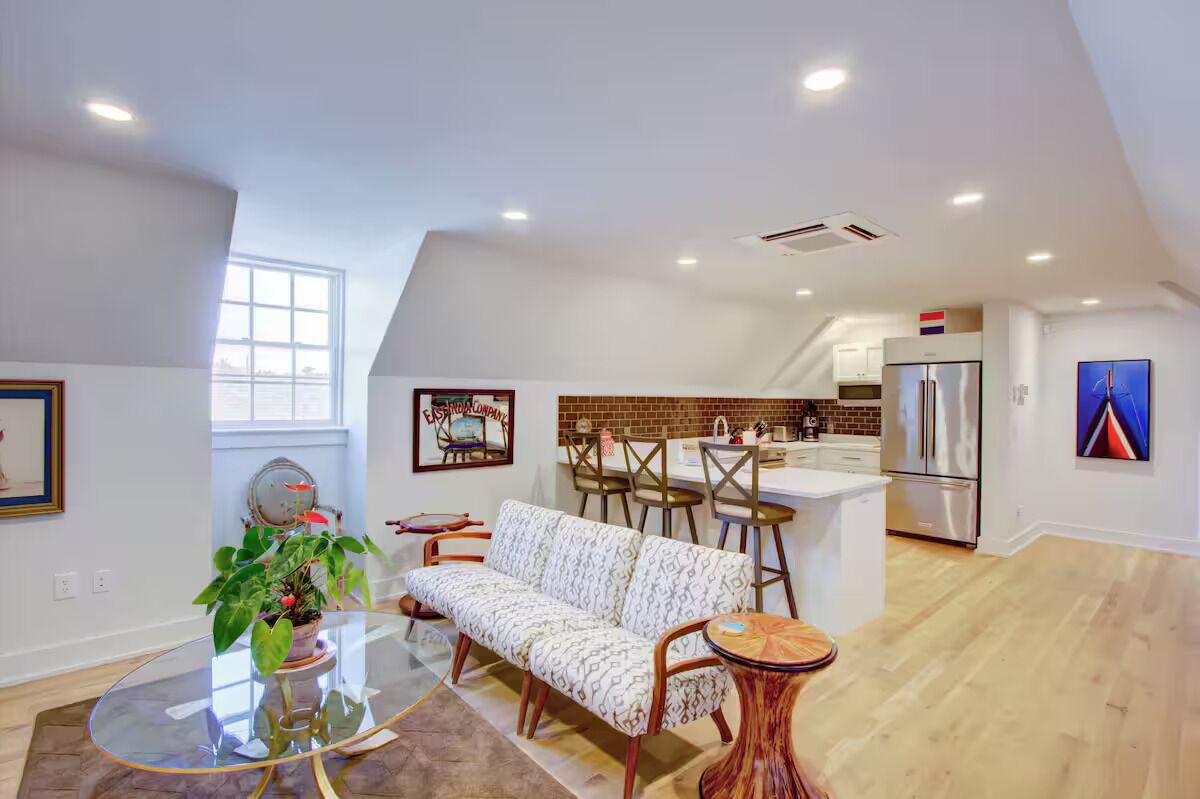 A modern kitchen with a refrigerator, a dining area with a sofa and chairs, and a large window providing natural light.