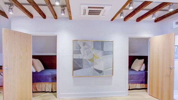 Quarto com duas camas, uma grande pintura abstrata e vigas de madeira no teto.