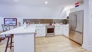 Uma cozinha moderna com armários brancos, geladeira de aço inoxidável e painel de azulejos.