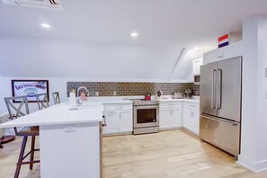 Eine moderne Küche mit weißen Schränken, einem Edelstahlkühlschrank und einer gefliesten Spritzschutzwand.