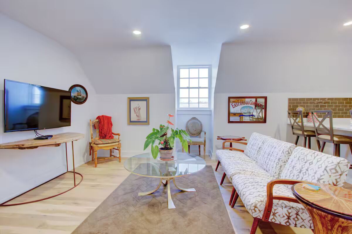 A modern living room with a flat-screen TV, a glass coffee table, a sofa, and a dining area with chairs and a table.