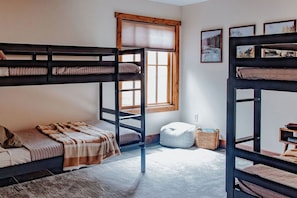 A bunk bed room with a window, a small ottoman, and a framed picture on the wall.
