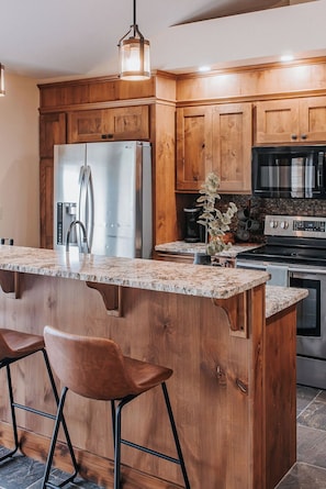 A modern kitchen with wooden cabinets, a stainless steel refrigerator, an oven, and a granite countertop.