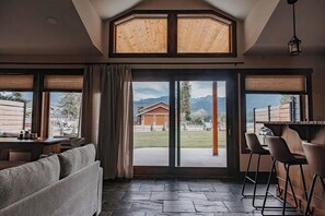 A modern interior with a large sliding glass door leading to an outdoor area, a bar area with stools, and a seating area with a sofa.