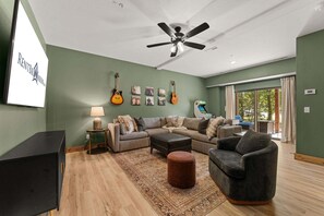 A living room with a sofa, ottoman, and a television on a stand. - Grand Ole Cabin has Arcades_Air Hockey_Peaceful View_Pvt Hot Tub_Near Pool & Lazy River (Hollister)