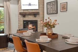 A dining area with a fireplace, a banner with a logo, and a table set for four with plates, cups, and a vase of flowers. - Grand Ole Cabin has Arcades_Air Hockey_Peaceful View_Pvt Hot Tub_Near Pool & Lazy River (Hollister)