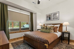 A bedroom with a large bed, two bedside lamps, a window with curtains, and two framed pictures on the wall. - Grand Ole Cabin has Arcades_Air Hockey_Peaceful View_Pvt Hot Tub_Near Pool & Lazy River (Hollister)