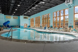 En pool med en blå vattenrutschkana, omgiven av solstolar och stora fönster.