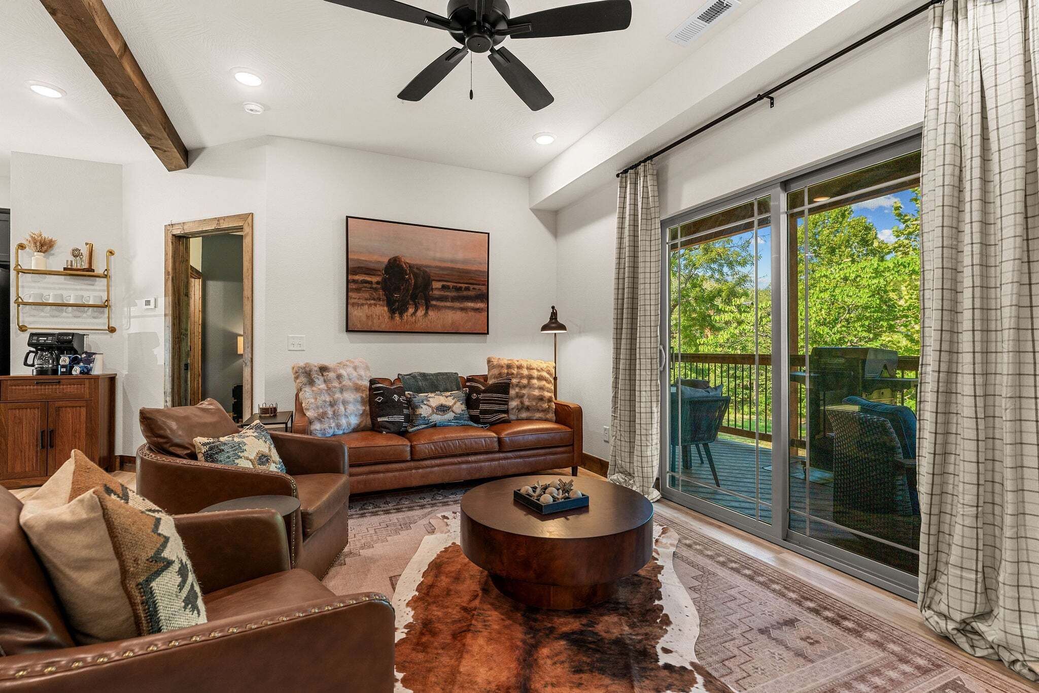A spacious living room with a leather sofa, a coffee table, and a large window offering a view of the outdoors.