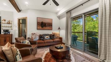 A spacious living room with a leather sofa, a coffee table, and a large window offering a view of the outdoors.