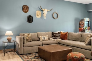 A living room with a sectional sofa, a coffee table, a lamp, and wall decorations including a cow skull and a deer head. - Yellowstone Cabin w Arcades_Air Hockey_Pvt Hot Tub_Great Community Amenities (Hollister)