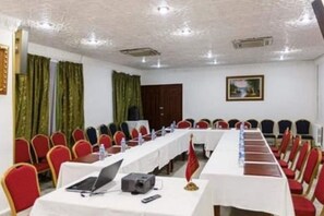 Un salón de conferencias con filas de mesas y sillas, equipado con computadoras portátiles y proyectores.