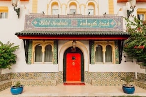 Entrada de hotel con puerta roja, un letrero con texto y azulejos decorativos.
