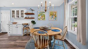 A dining area with a round table, chairs, a chandelier, and artwork on the walls. - Sweetgrass Cottage, Pond Views, Pet Friendly, Boat Trailer Parking & Fireplace (Georgetown)