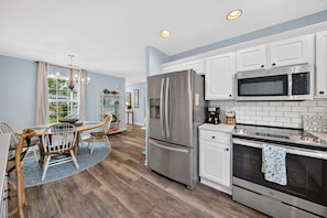 A modern kitchen with stainless steel appliances, white cabinetry, and a dining area with a wooden table and chairs. - Sweetgrass Cottage, Pond Views, Pet Friendly, Boat Trailer Parking & Fireplace (Georgetown)