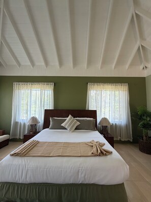 A hotel room with a large bed, two bedside tables, a nightstand, a potted plant, and a window with curtains.