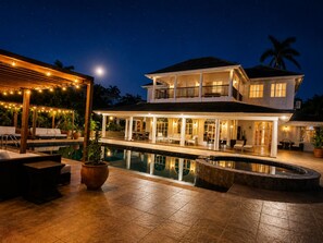 A two-story house with a swimming pool, outdoor seating, and string lights.