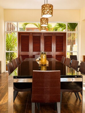 Un comedor con una mesa de vidrio rodeada de sillas, un jarrón decorativo y un separador de madera con contraventanas.