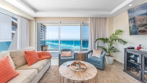 A modern living room with a view of the ocean, a sofa, two armchairs, a coffee table, and a potted plant. - Verano 1601 – Spacious Corner Condo (Puerto Peñasco)