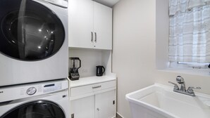Uma área de lavanderia compacta com máquina de lavar, secadora, cafeteira e pia.