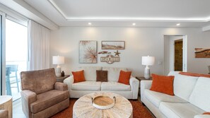 Una sala de estar con un sillón marrón, un sofá beige y una mesa de centro redonda con una bandeja decorativa.