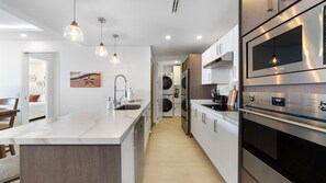 Una cocina moderna con una isla central, electrodomésticos de acero inoxidable, iluminación colgante y vistas al área de estar contigua.