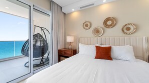 Habitación de hotel con cama, mesita de noche, lámpara, una silla colgante y vistas al mar.