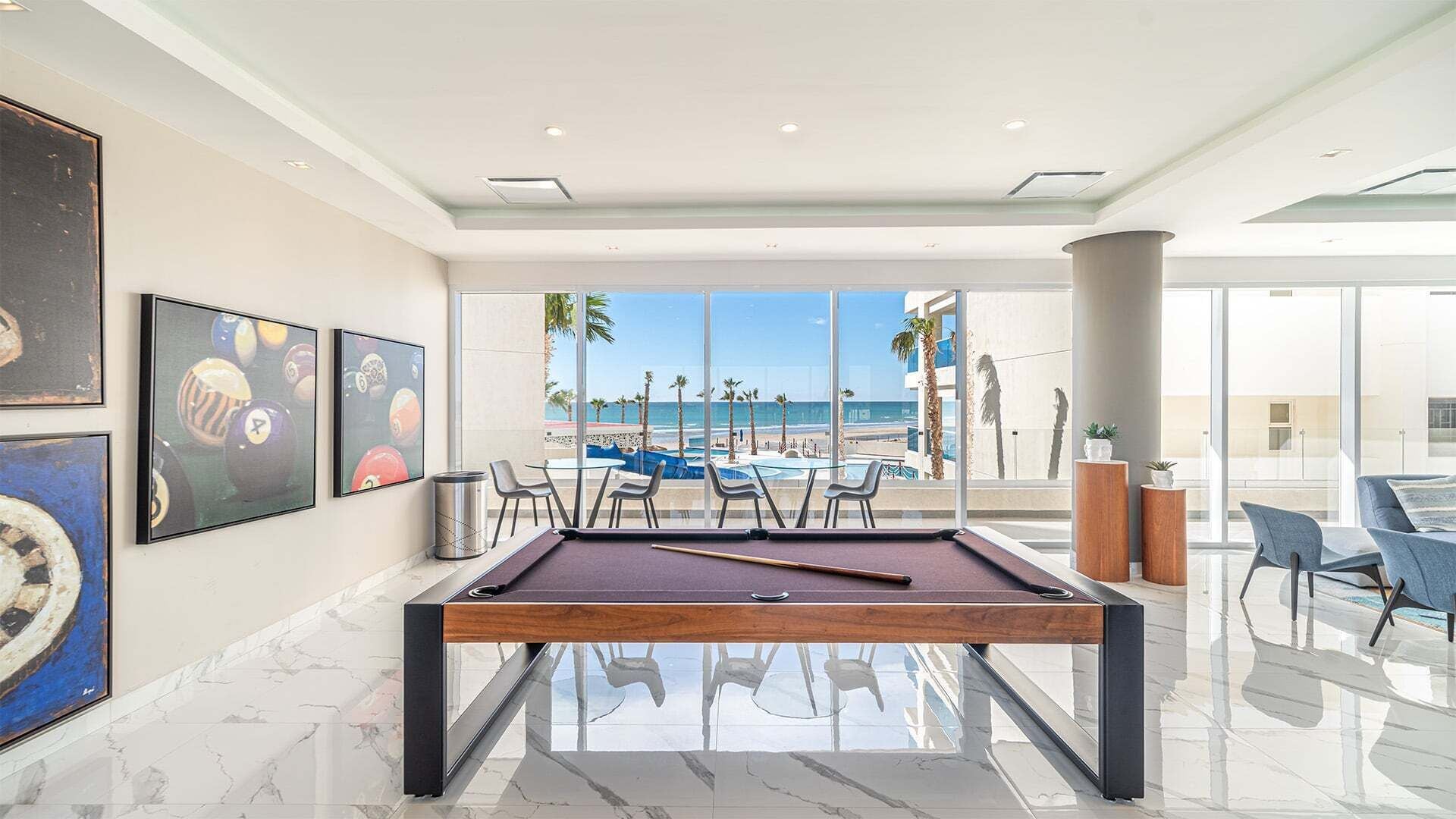 A pool table with a view of the beach, framed artwork, and modern furniture.
