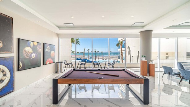 Mesa de bilhar com vista para a praia, obras de arte emolduradas e mobiliário moderno.