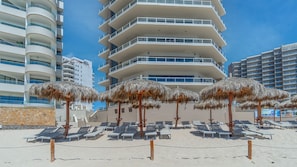 Um hotel à beira-mar com várias varandas, espreguiçadeiras e guarda-sóis de palha.