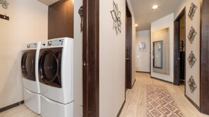 A laundry room with two front-loading washers and dryers, a wooden door, and a patterned rug on the floor. - Las Palomas Phase II Coronado 506 Exceptional Oceanfront 2BR 2BA Unit. (Puerto Peñasco)