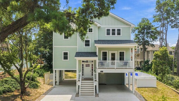 A two-story building with a front porch, a garage, and a covered driveway. - Out of Office OBX | Private Pool, Hot Tub, Dog Friendly, and Community Pool (Corolla)