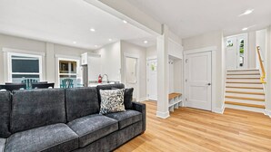 A modern living room with a grey sofa, wooden flooring, and a staircase leading to an upper level. - Out of Office OBX | Private Pool, Hot Tub, Dog Friendly, and Community Pool (Corolla)