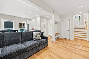 Ein modernes Wohnzimmer mit grauem Sofa, Holzboden und einer Treppe, die zu einer oberen Ebene führt.