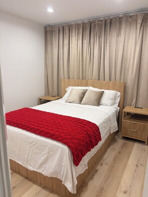 Una camera da letto con una testiera in legno, biancheria da letto bianca, una coperta rossa e un comodino in legno con cassetti.