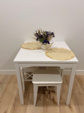 Ein weißer Tisch mit zwei gewebten Tischsets und einer Vase mit getrockneten Blumen.