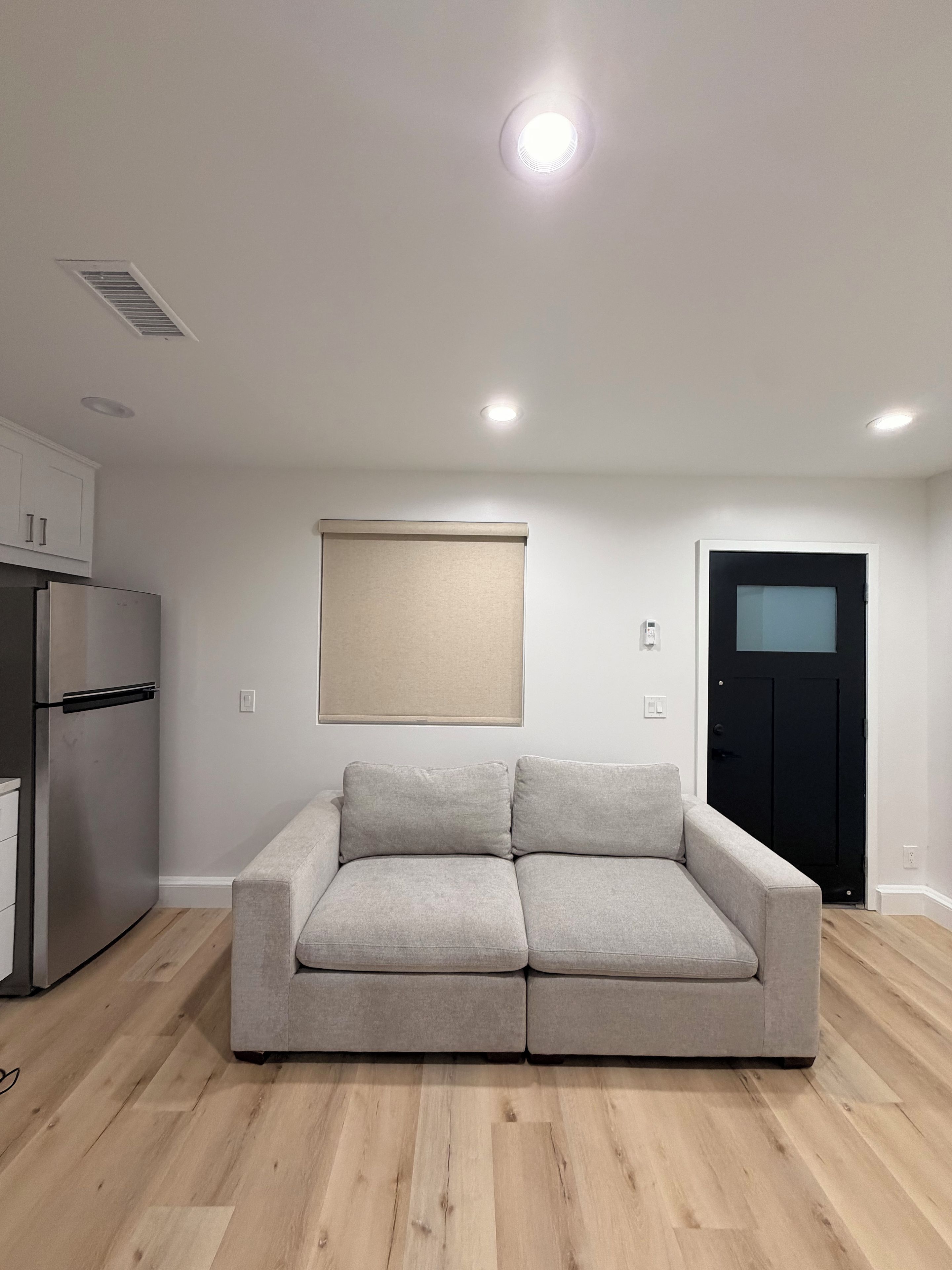 A modern kitchen with a built-in refrigerator, a light-colored sofa, and a black door.